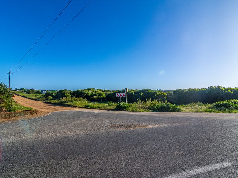 A view of the intersection showing an asphalt road meeting a dirt access path, with surrounding natural vegetation and utility infrastructure.