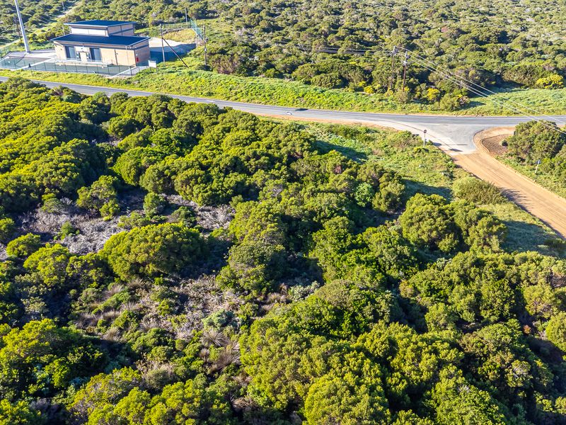 Aerial view of a vacant commercial land plot featuring natural vegetation, adjacent road access, and a nearby utility structure.