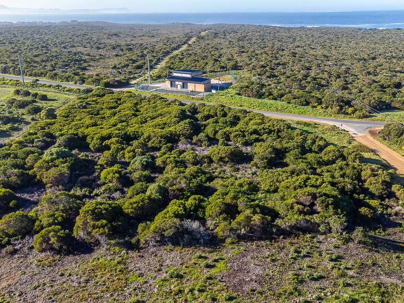 Aerial view of a vacant commercial land plot featuring natural vegetation, a small utility building, and established road access near the coastline.