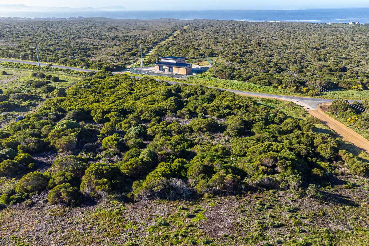 Aerial view of a vacant commercial land plot featuring natural vegetation, a small utility building, and established road access near the coastline.