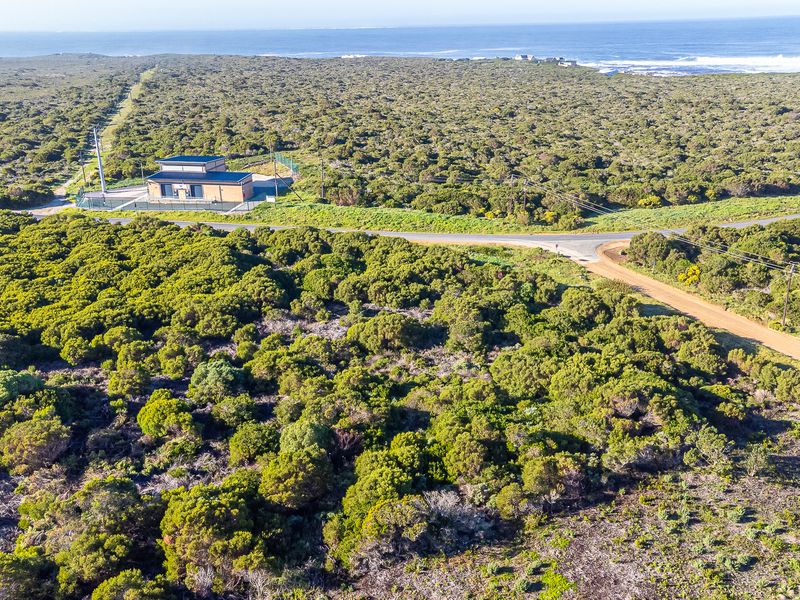 Aerial view of a commercial vacant land plot featuring a utility building, access roads, and coastal landscape surroundings.