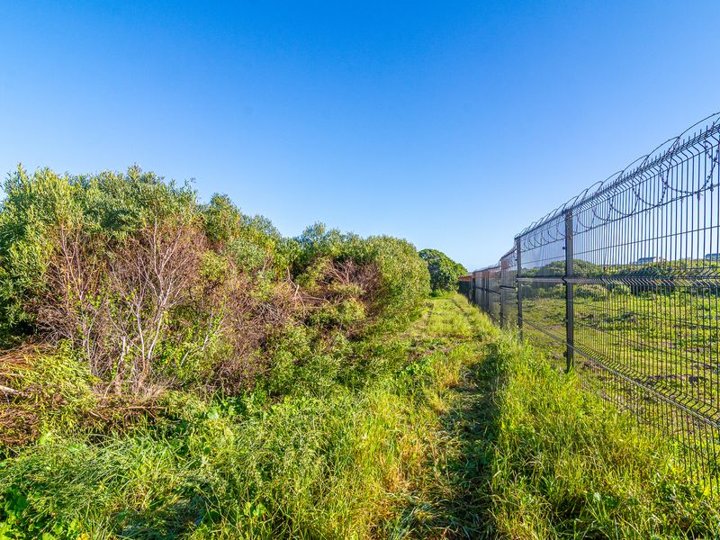 A view of the vacant commercial land featuring established vegetation and secure perimeter fencing with barbed wire topping.