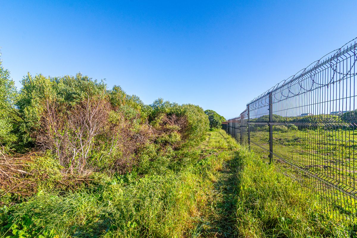 A view of the vacant commercial land featuring established vegetation and secure perimeter fencing with barbed wire topping.