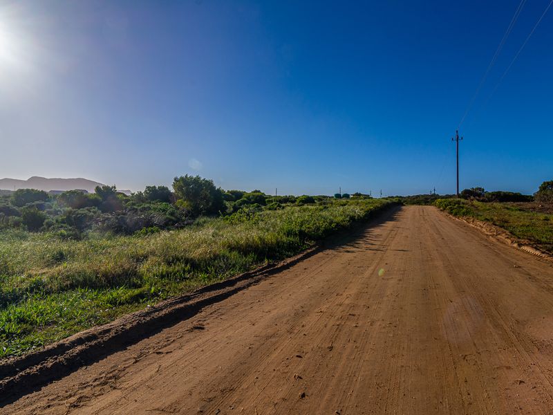 A view of a dirt access road leading through vacant land with a utility pole and overhead power lines visible.