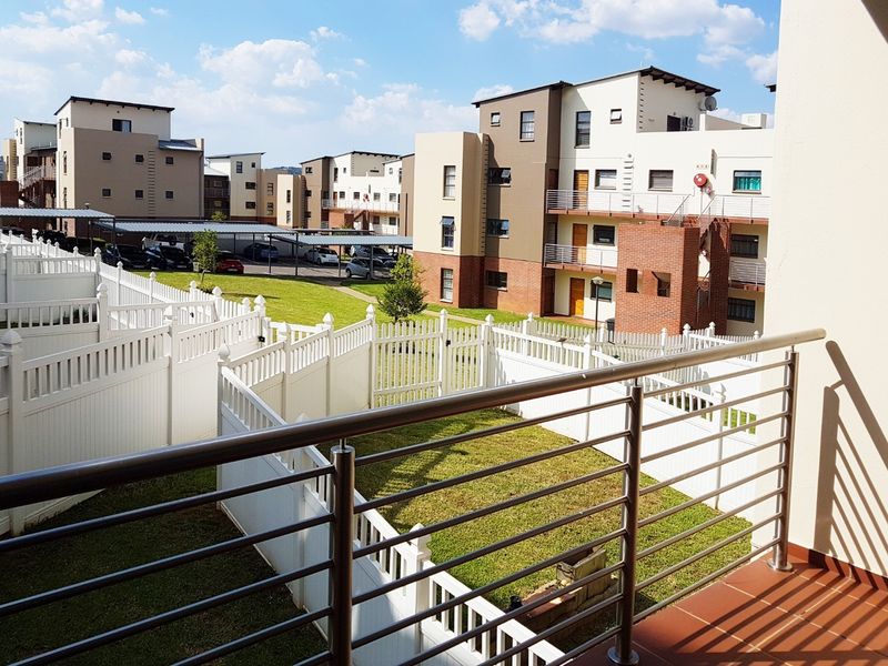 A view from a balcony overlooking a well-maintained communal garden area and apartment complex grounds with covered parking.