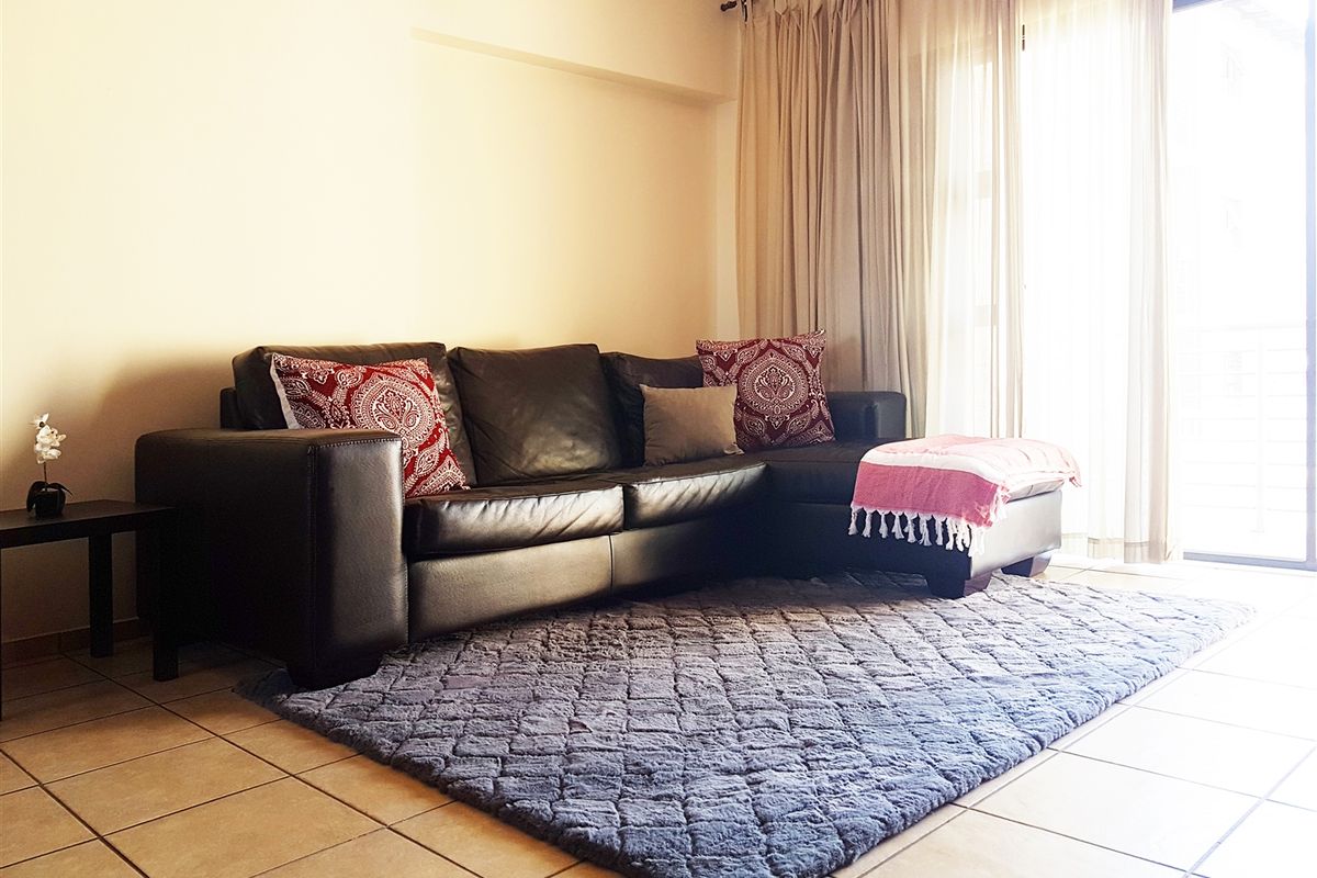 A living room featuring neutral tiled flooring and a large sliding glass door with curtain tracks, providing access to an outdoor area.