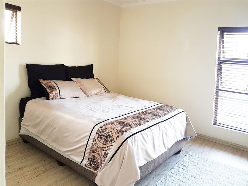 A bright bedroom featuring light-toned laminate flooring and dual windows fitted with venetian blinds, offering a neutral canvas for personalization.