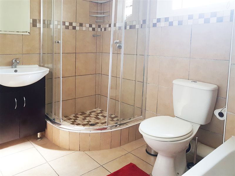 A functional bathroom featuring a corner shower enclosure, vanity basin, and toilet with neutral wall and floor tiling.