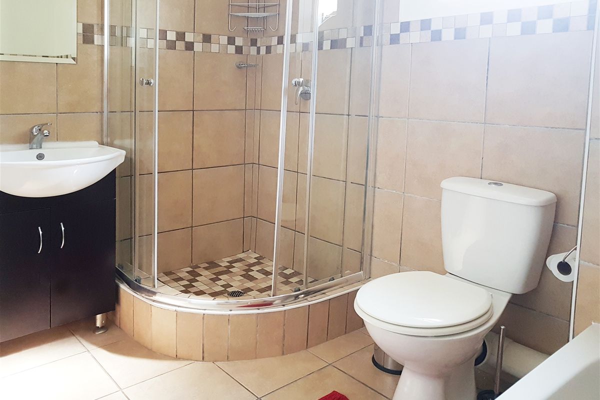 A functional bathroom featuring a corner shower enclosure, vanity basin, and toilet with neutral wall and floor tiling.