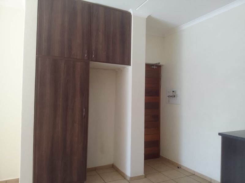 A clean, empty bedroom featuring built-in dark wood cupboards, tiled flooring, and a solid wooden door.