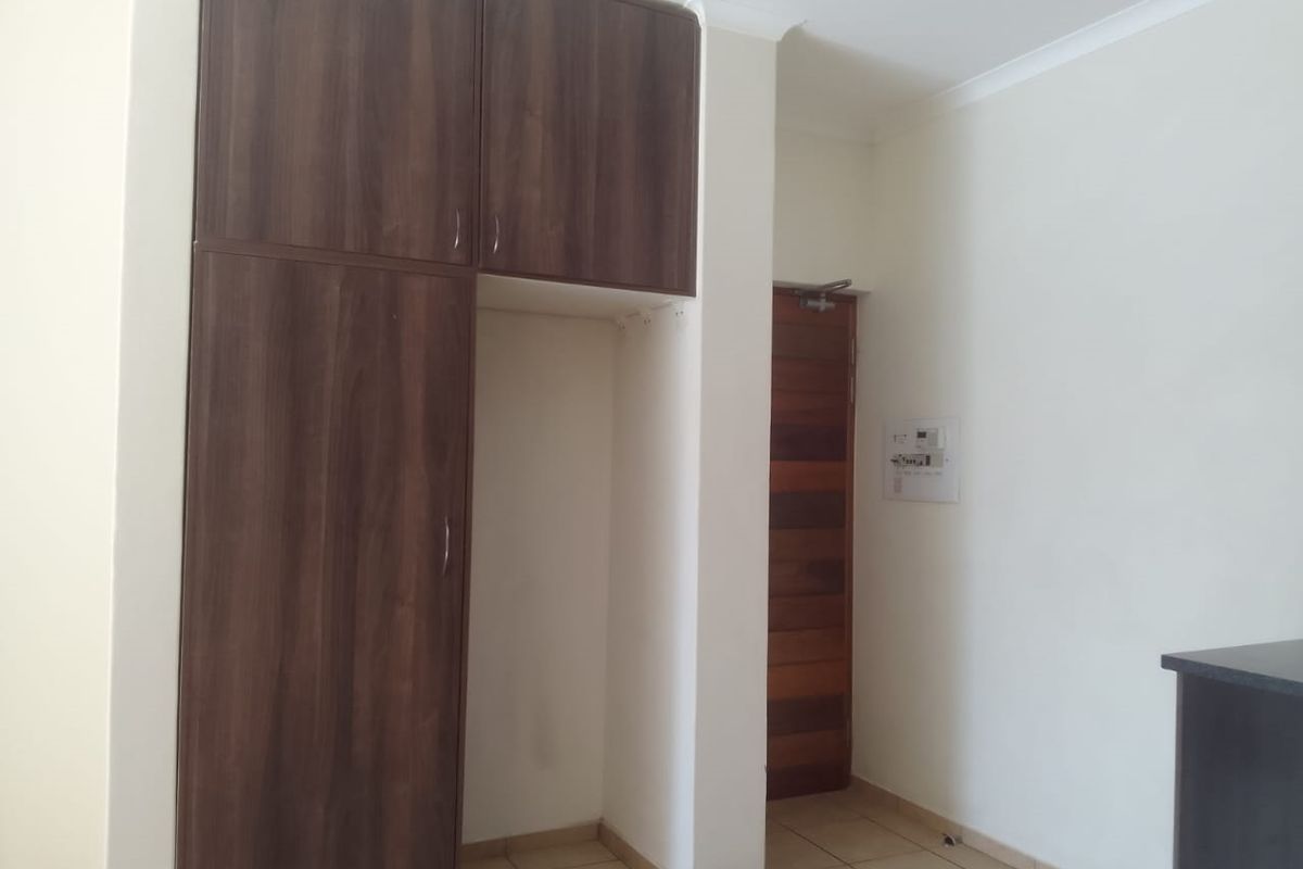 A clean, empty bedroom featuring built-in dark wood cupboards, tiled flooring, and a solid wooden door.