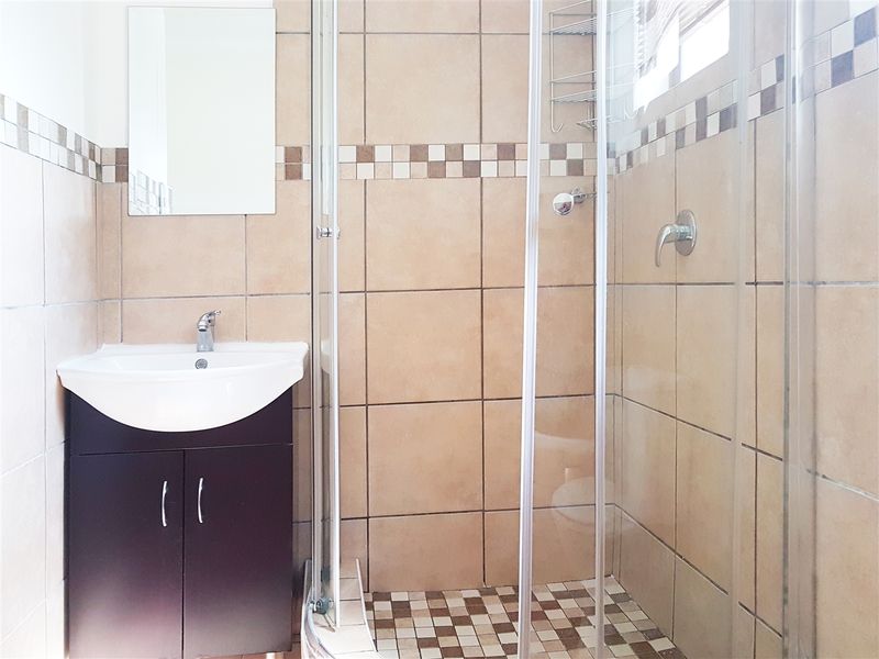 A functional bathroom featuring a vanity cabinet with a basin, a glass shower enclosure, and neutral-toned wall tiling with decorative mosaic accents.