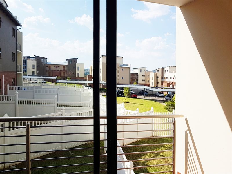 A balcony with a stainless steel balustrade offering views over the apartment complex grounds and parking area.