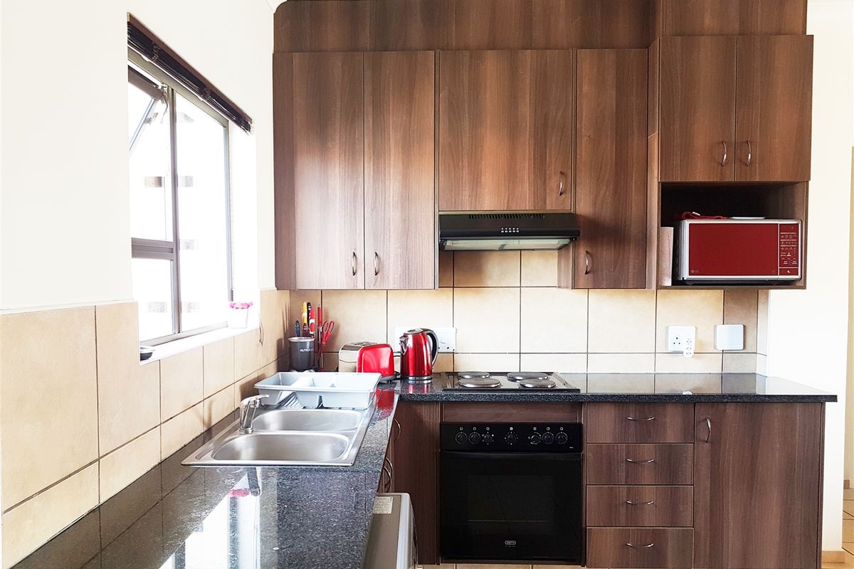 A functional kitchen featuring dark wood cabinetry, granite countertops, a built-in oven with hob, and a stainless steel double sink with tiled backsplash.