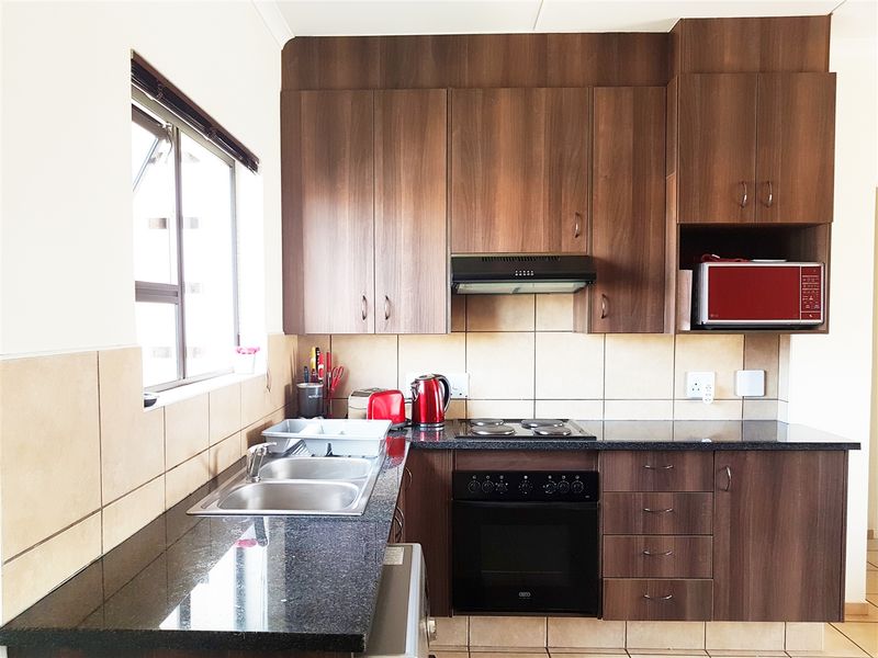 A functional kitchen featuring dark wood cabinetry, granite countertops, a built-in oven with hob, and a stainless steel double sink with tiled backsplash.