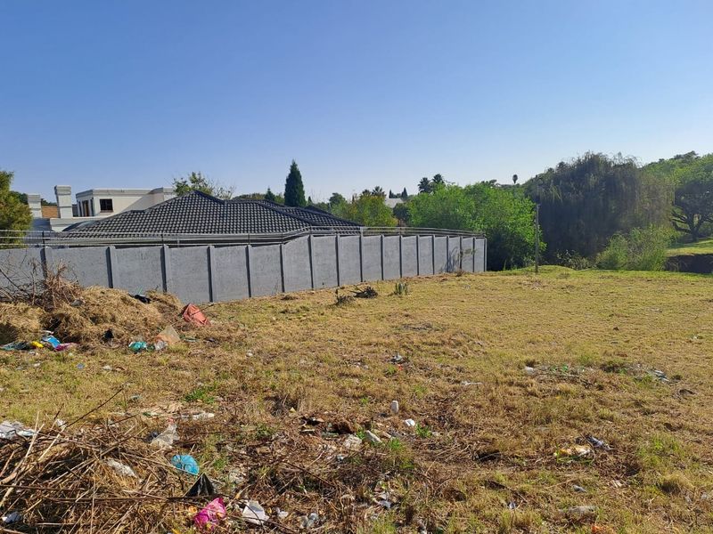 A vacant residential plot featuring a precast concrete boundary wall and metal security fencing, currently requiring site clearing of accumulated debris.