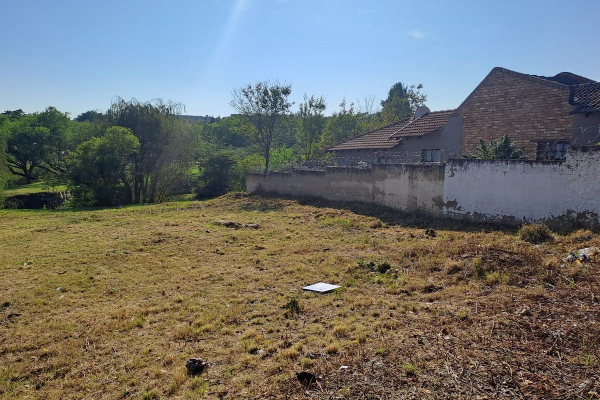 A view of a vacant residential plot featuring a perimeter wall with security razor wire and surrounding greenery.