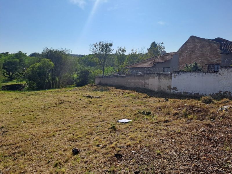 A view of a vacant residential plot featuring a perimeter wall with security razor wire and surrounding greenery.