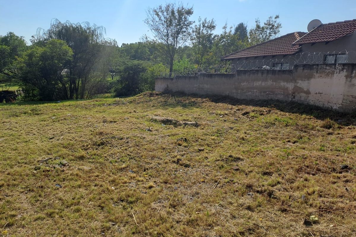 A vacant residential plot featuring a perimeter wall with security razor wire and mature trees in the background.