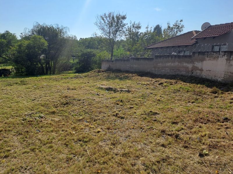 A vacant residential plot featuring a perimeter wall with security razor wire and mature trees in the background.