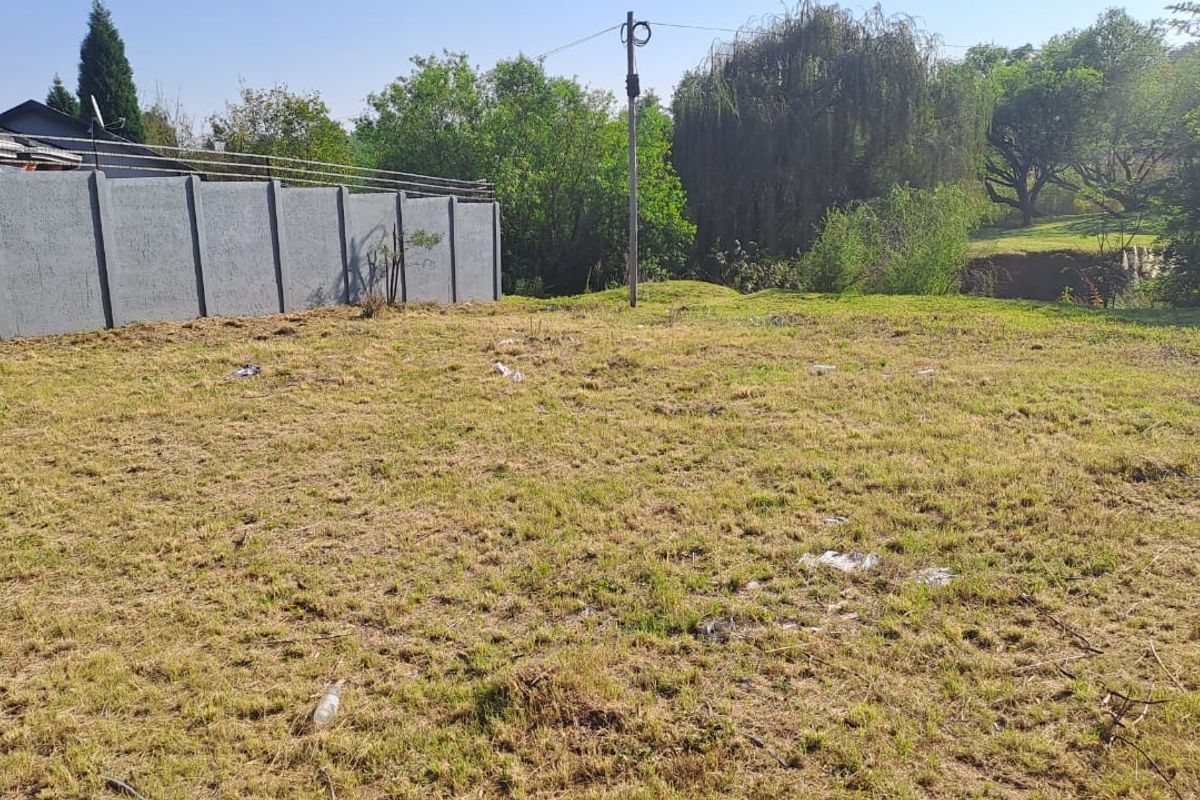 A vacant residential plot featuring a precast concrete boundary wall and established trees in the background.
