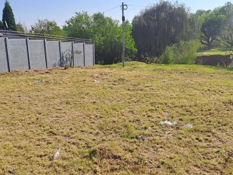 A vacant residential plot featuring a precast concrete boundary wall and established trees in the background.
