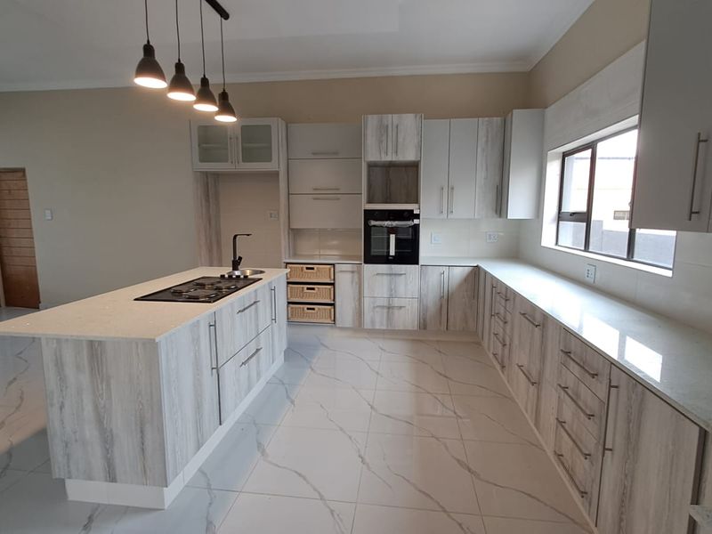 Modern kitchen featuring light wood-grain cabinetry, stone countertops, a central island with a gas hob, built-in oven, and polished porcelain floor tiles.