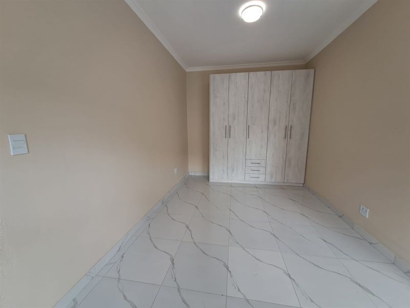 A clean, empty bedroom featuring modern marble-look tiled flooring and a large, light-toned built-in wardrobe.