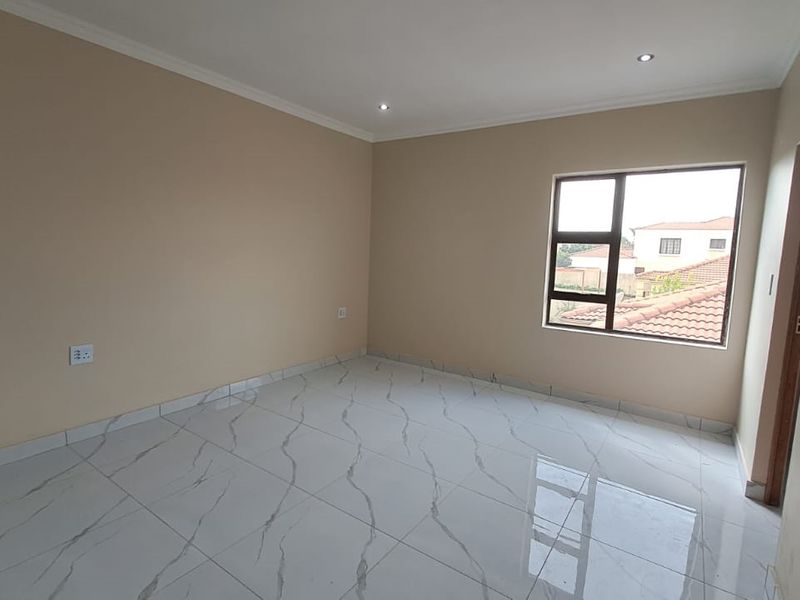 A bright, empty bedroom featuring modern marble-look floor tiles, neutral wall paint, and recessed downlighting.