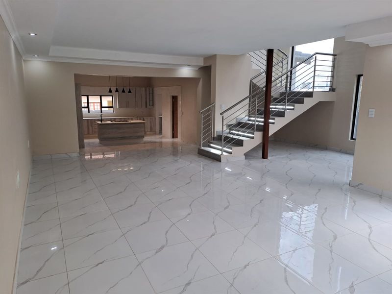 Spacious open-plan living area featuring polished marble-look floor tiles, a modern staircase with integrated lighting, and a contemporary kitchen with a central island.