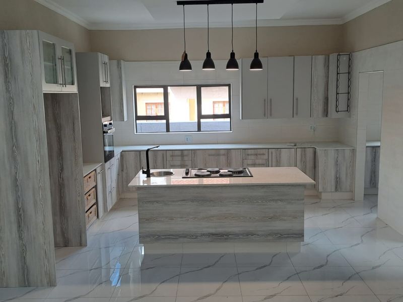 Modern kitchen featuring a central island with a gas hob, stone countertops, light wood-grain cabinetry, and polished marble-look tiled flooring.