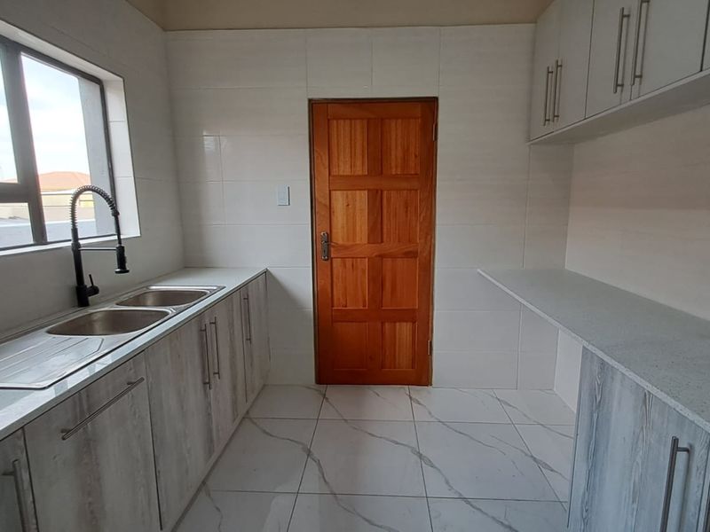 A clean, modern scullery featuring quartz countertops, double sink with gooseneck faucet, ample built-in cabinetry, and neutral tiled finishes.