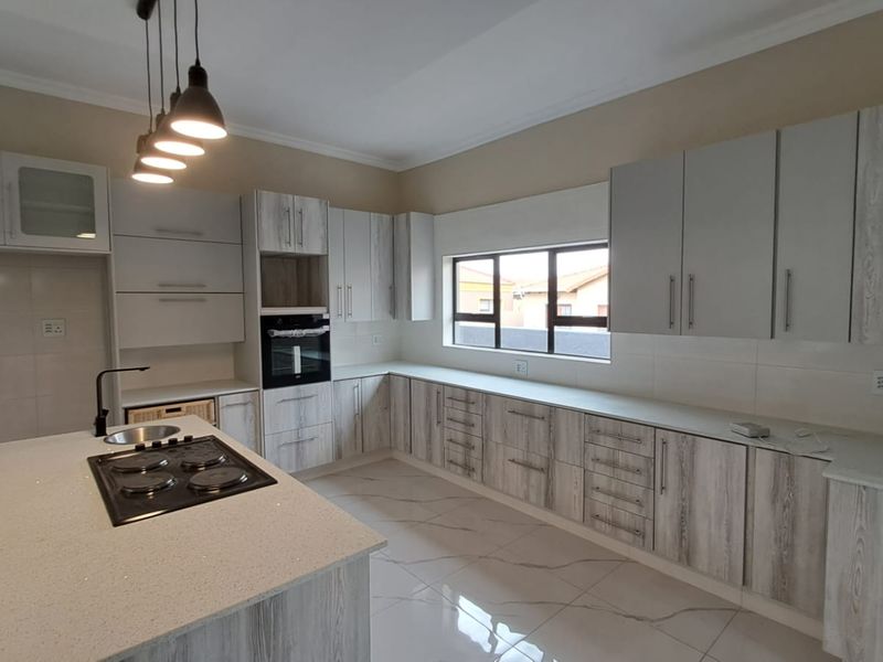 Modern kitchen featuring light wood-grain cabinetry, stone countertops, a central island with a built-in hob, and high-quality tiled flooring.