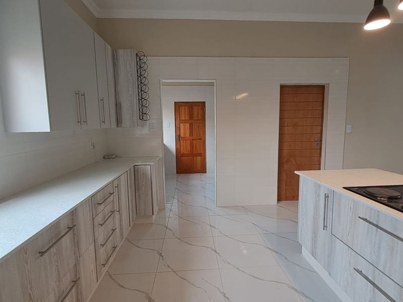 Modern kitchen featuring light wood-grain cabinetry, stone countertops, a central island with an integrated hob, and polished marble-look floor tiles.