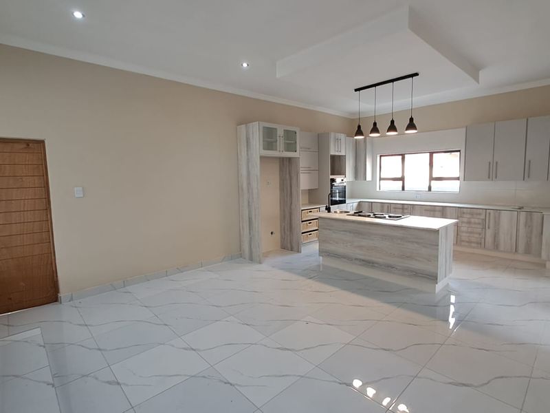 Spacious open-plan kitchen featuring modern light-wood cabinetry, a central island with a built-in hob, and sleek tiled flooring throughout.