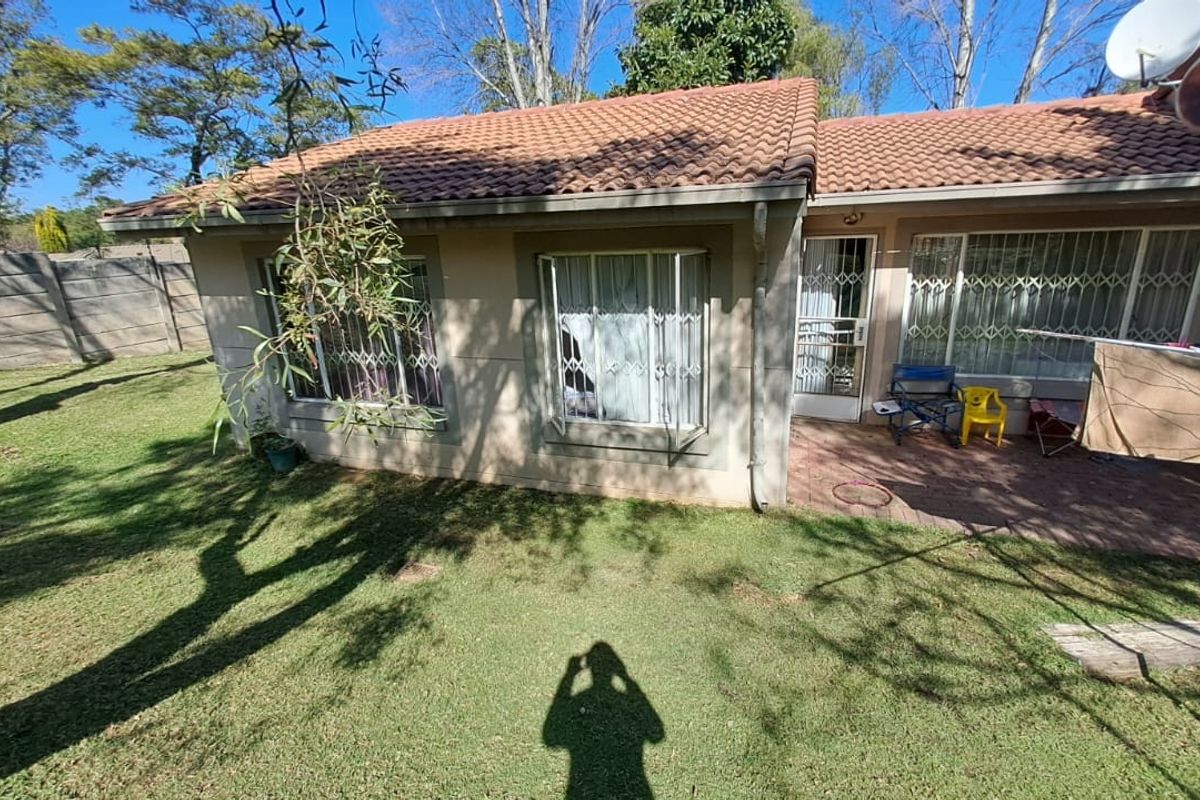 Rear view of the townhouse featuring a tiled roof, paved patio area, and security gates on windows and doors, set within a private garden.