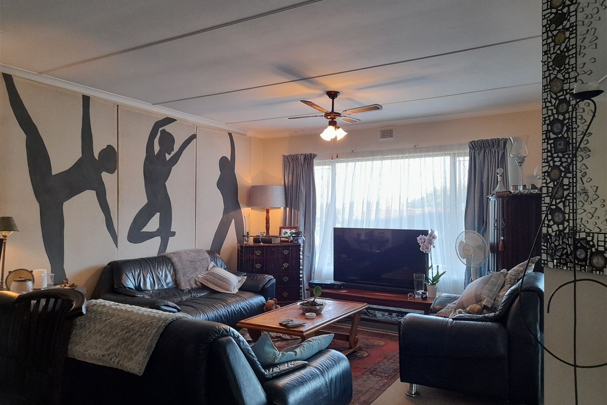A comfortable living room featuring a ceiling fan, large window for natural light, and a tiled ceiling finish.