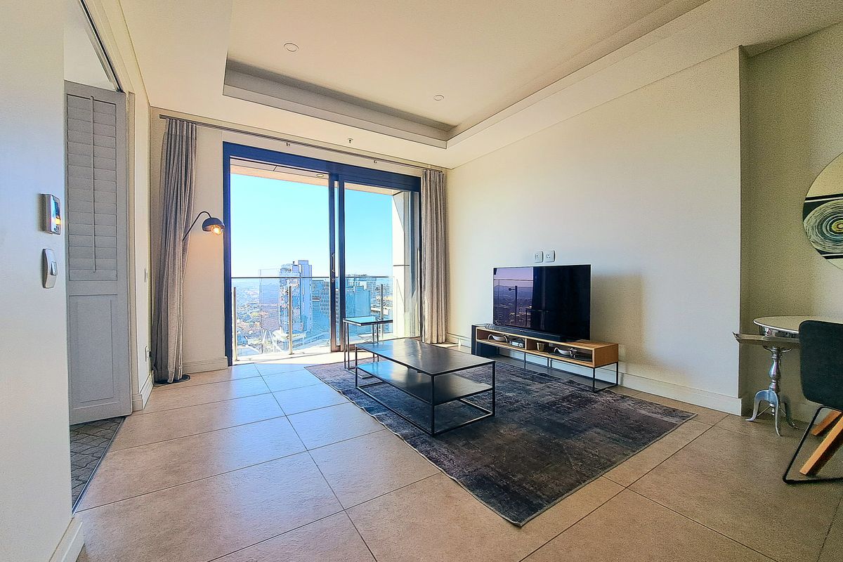 Modern living room featuring large sliding glass doors leading to a balcony with city views, recessed ceiling lighting, and neutral tiled flooring.