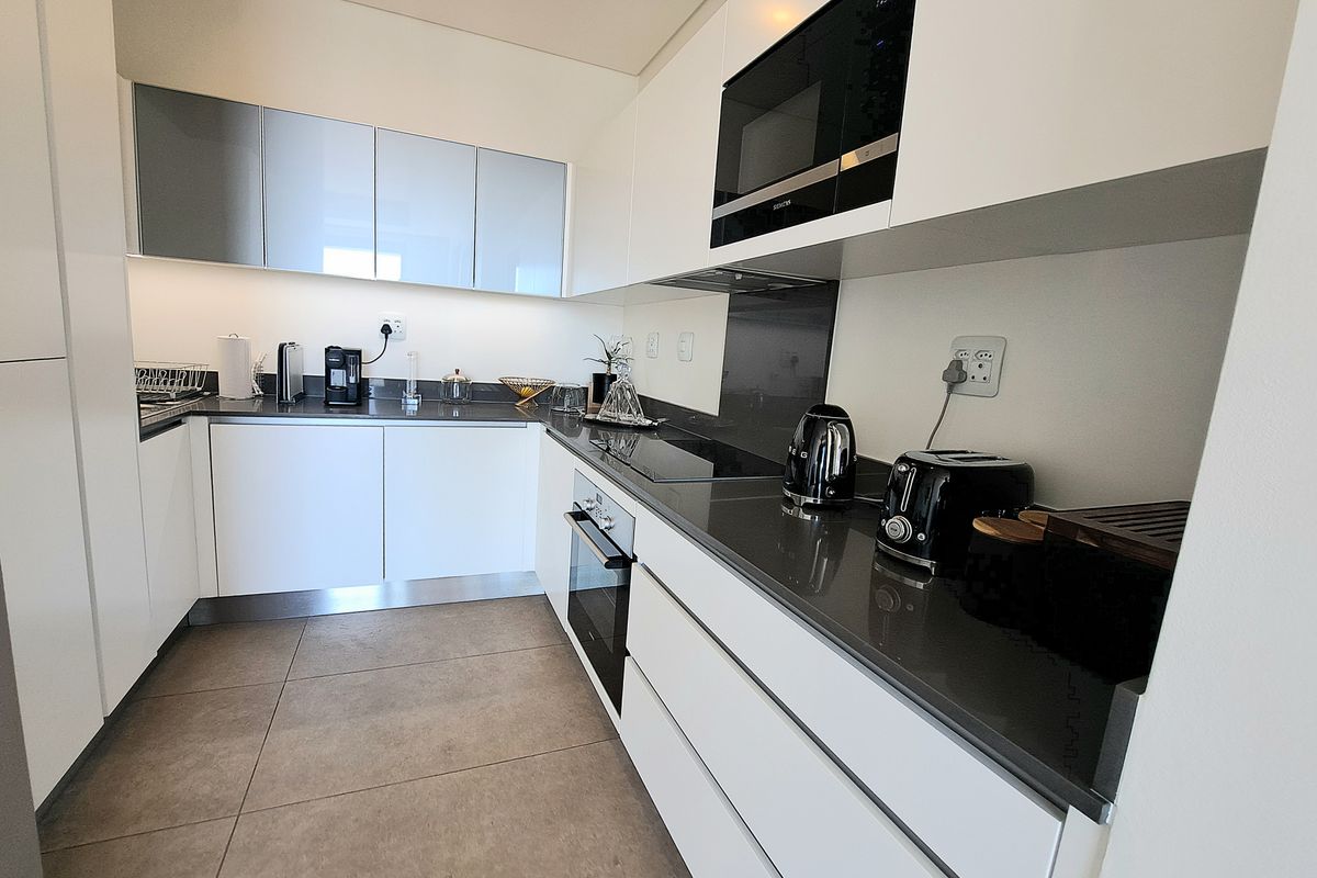 Modern kitchen featuring sleek white cabinetry, dark stone countertops, integrated appliances, and high-quality tiled flooring with efficient under-cabinet lighting.