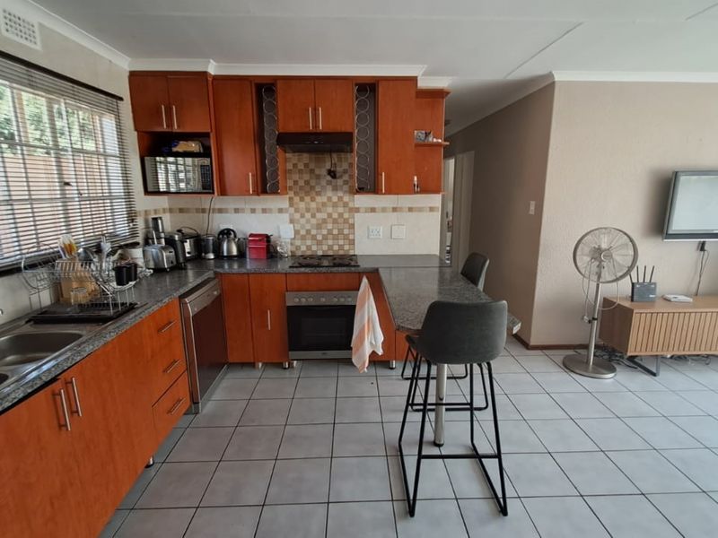 Open-plan kitchen and living area featuring wooden cabinetry, granite countertops, built-in oven, gas hob, and tiled flooring throughout.