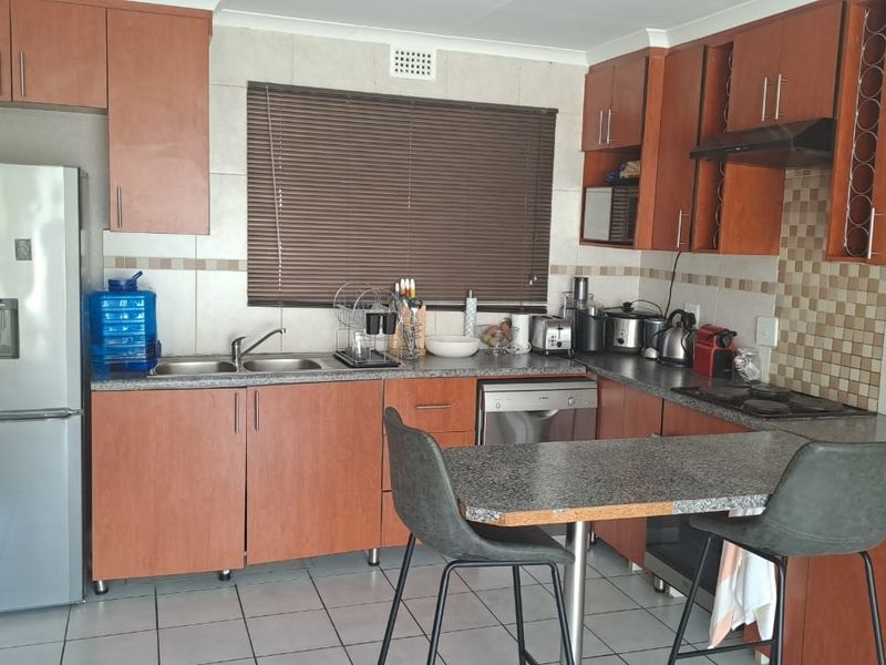 A functional kitchen featuring wood-look cabinetry, tiled splashbacks, a breakfast bar, and integrated appliances, offering a practical layout for daily meal preparation.