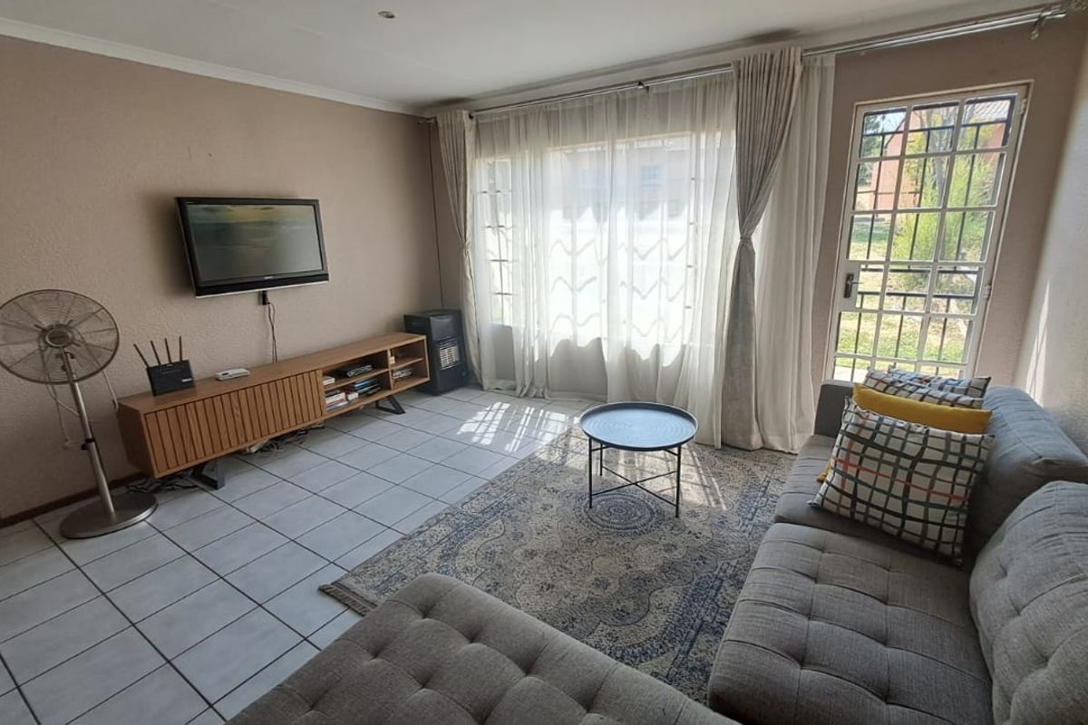 A living room featuring tiled flooring, large windows with curtains, and a security gate providing access to the exterior.