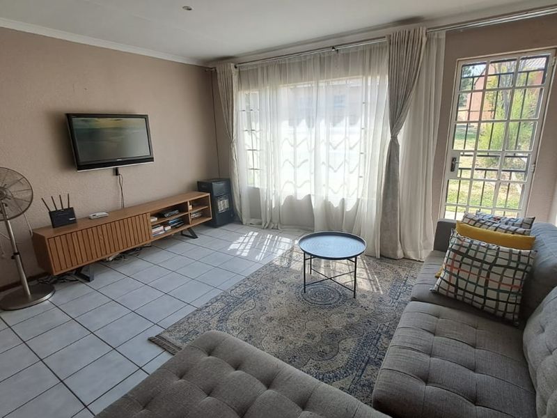A living room featuring tiled flooring, large windows with curtains, and a security gate providing access to the exterior.