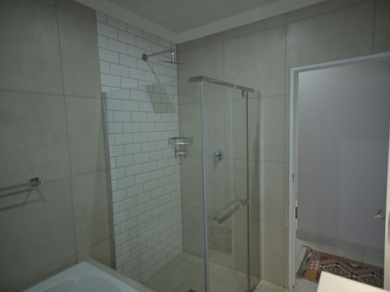 Modern bathroom featuring a glass-enclosed shower with subway tile accents, a rain shower head, and neutral large-format wall tiles.