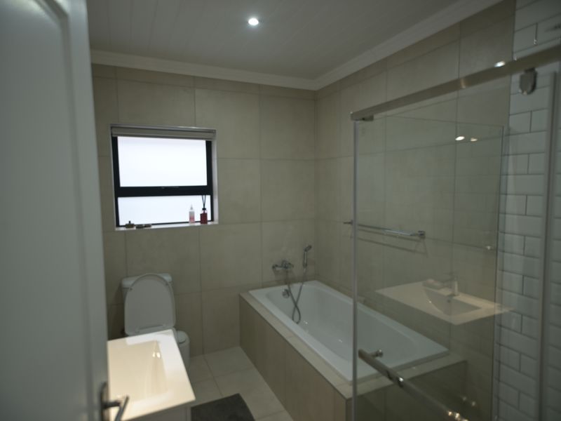 Modern bathroom featuring a built-in bathtub, glass shower enclosure, vanity basin, and neutral wall tiling with recessed lighting.