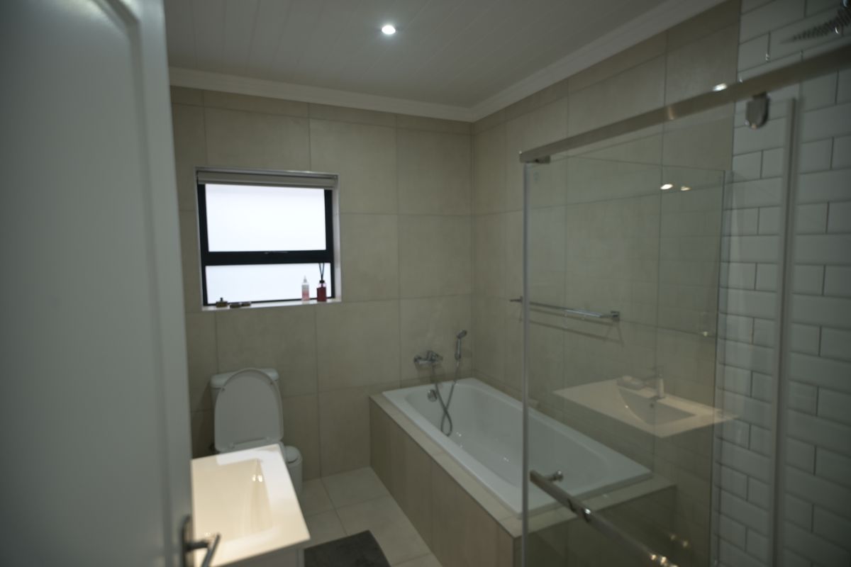 Modern bathroom featuring a built-in bathtub, separate glass shower enclosure, vanity basin, and neutral wall tiling.