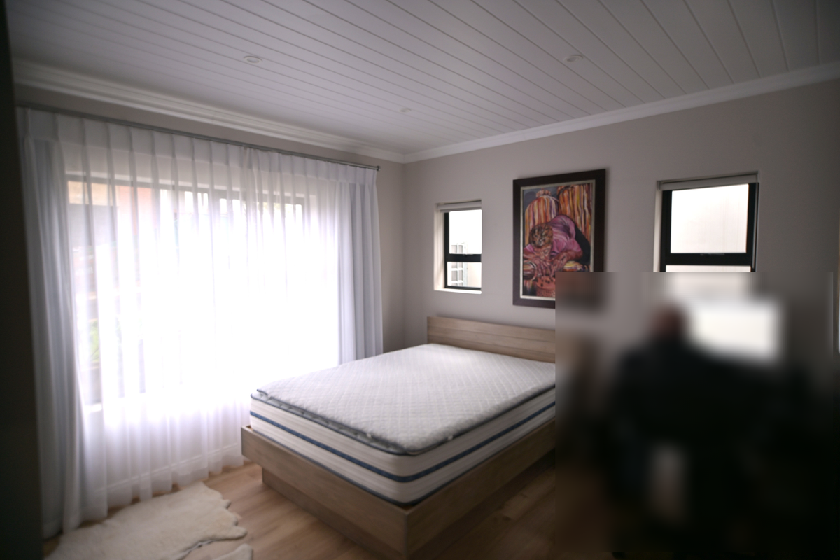 A well-maintained bedroom featuring timber flooring, a tongue and groove ceiling with recessed lighting, and large windows with curtain tracks.
