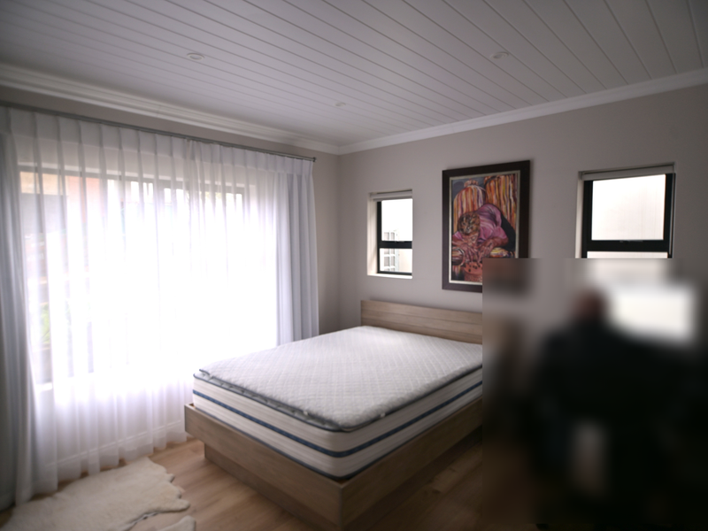 A well-maintained bedroom featuring timber flooring, a tongue and groove ceiling with recessed lighting, and large windows with curtain tracks.