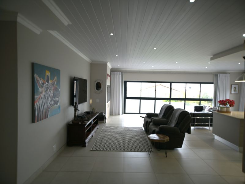 Spacious open-plan living area featuring tiled floors, a modern tongue and groove ceiling with recessed lighting, and large windows providing ample natural light.