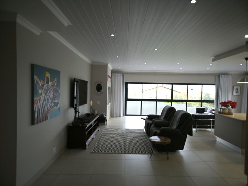 Spacious open-plan living area featuring tiled floors, recessed downlights, and a distinctive tongue and groove ceiling with large windows providing natural light.